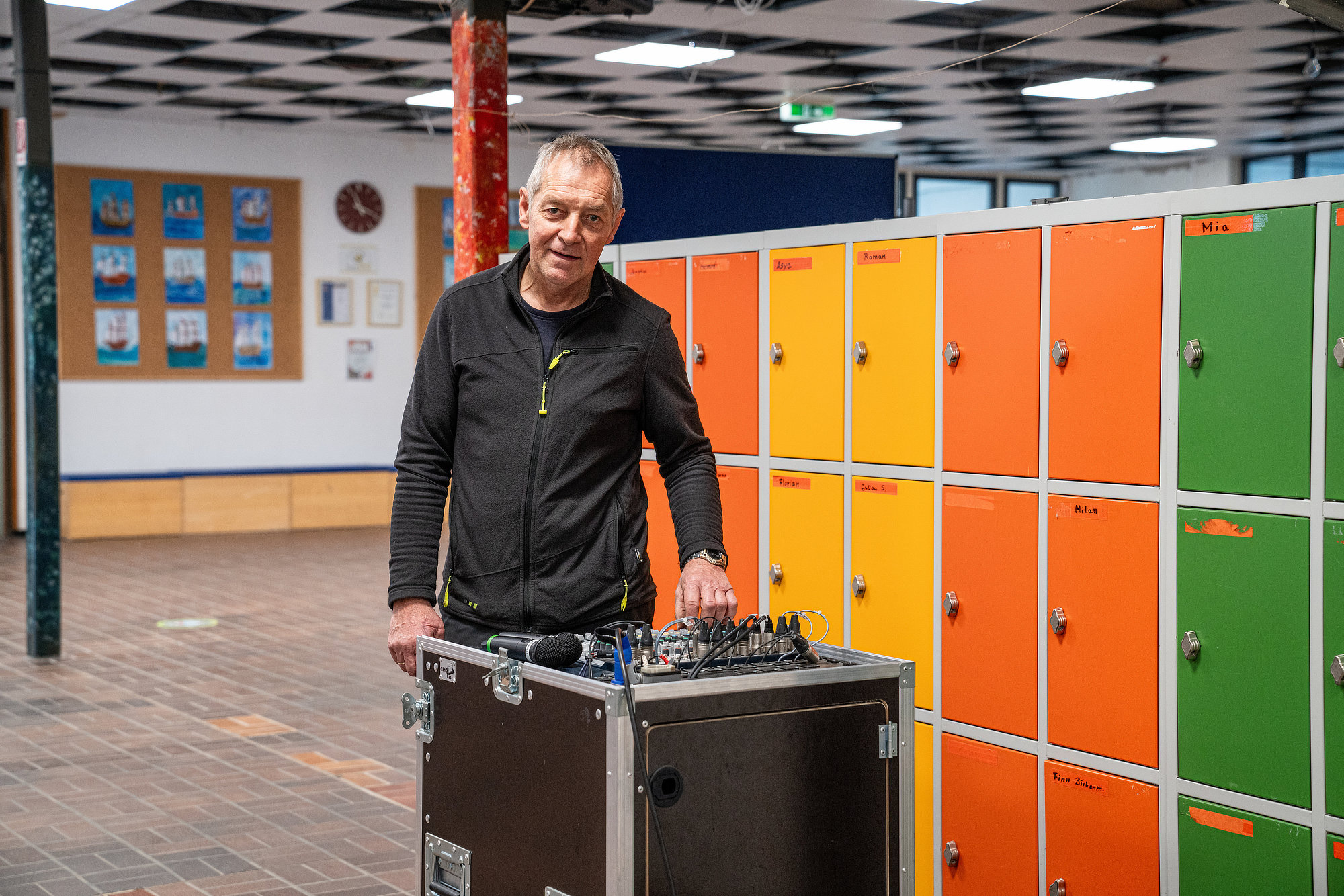 Der Hausmeister steht neben großem Gerät vor bunten Spinden