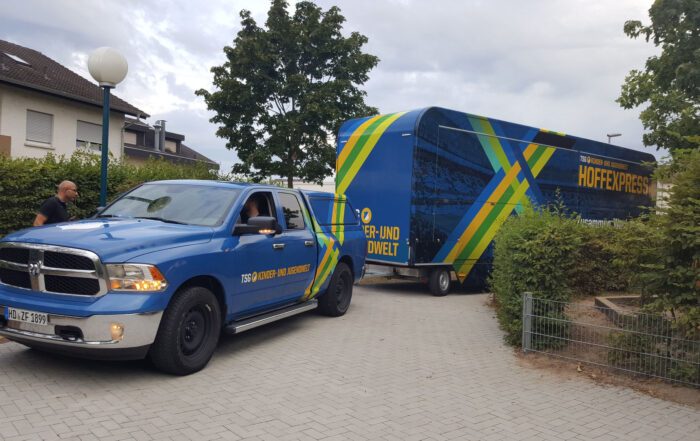 Ein blauer Last Wagen mit einem großen Anhänger steht vor einem Haus