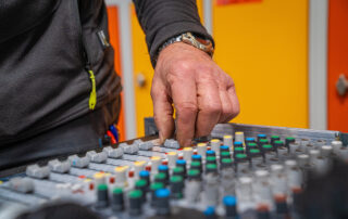 Finger am Mischpult mit Knopf und bunten Reglern