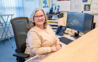 Frau Roth mit glücklichem Gesicht sitzt vor großem Monitor