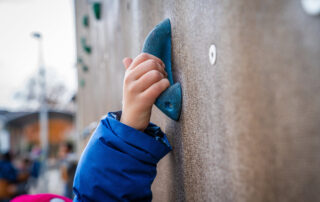 Kinderhand hält blauen Kletterstein an der Wand