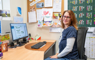 Konrektorin Herzer sitzt am Schreibtisch und schaut in die Kamera vor Bilderwand