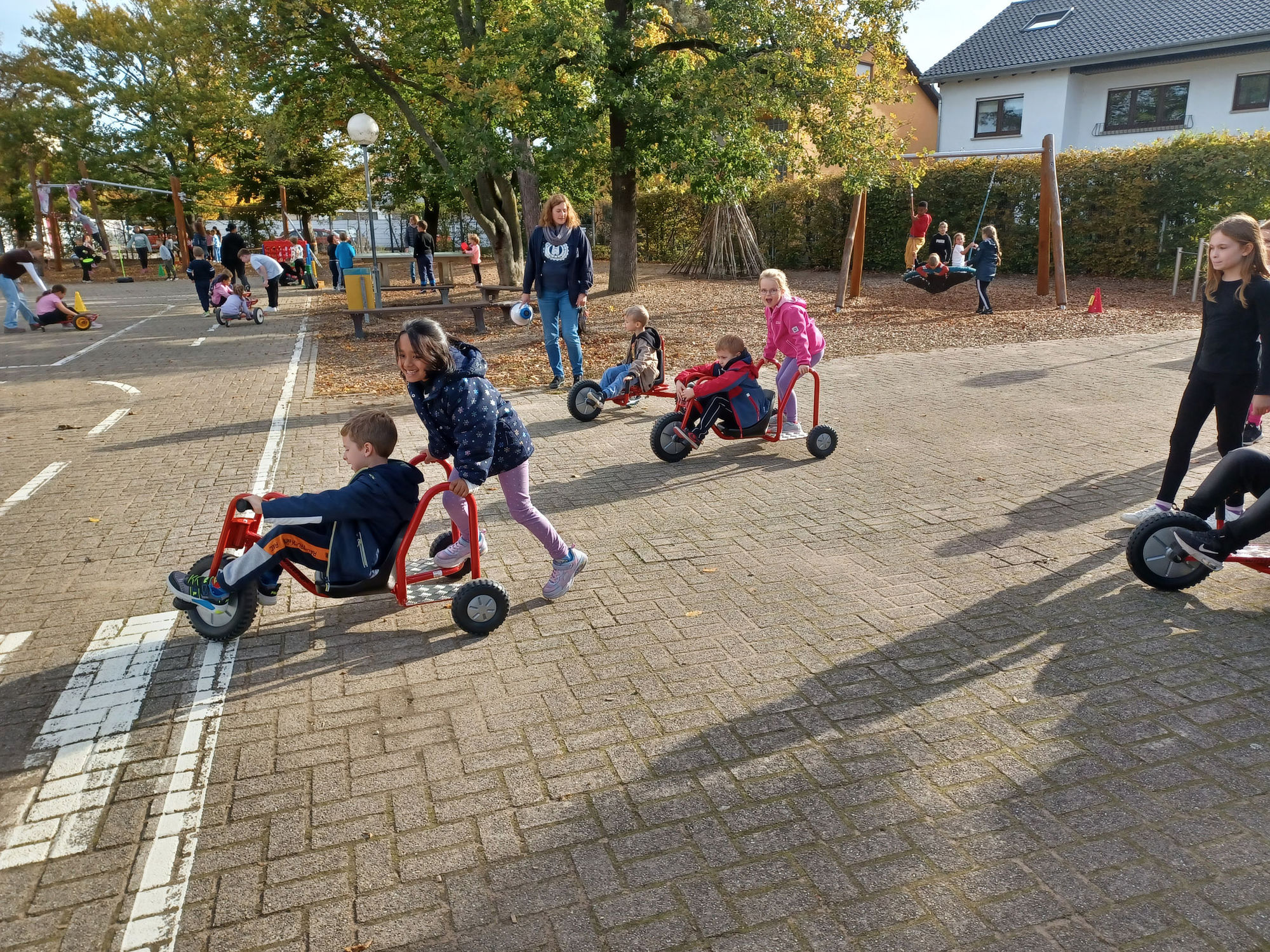 Mehrere Kinder fahren mit roten Dreirädern auf dem Schul Hof und haben Spass