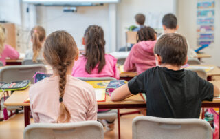 Rücken von Kindern im Klassenraum an Schülertischen